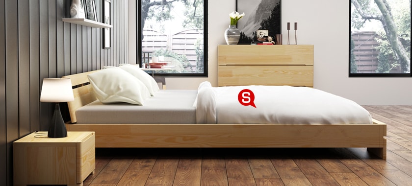 Przytulna sypialnia z dużym drewnianym łóżkiem. Szafka nocna oraz komoda z jasnego drewna doskonale podkreśla całą aranżację.